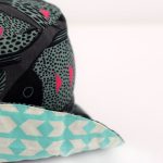 Gorro tipo pescador, en original estampado de peces en negro, gris y fucsia, por un lado y geométrico turquesa por el otro.