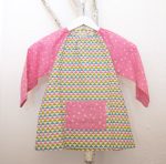 Bata para guardería, con estampado de triángulos y mangas y bolsillo delantero en rosa.